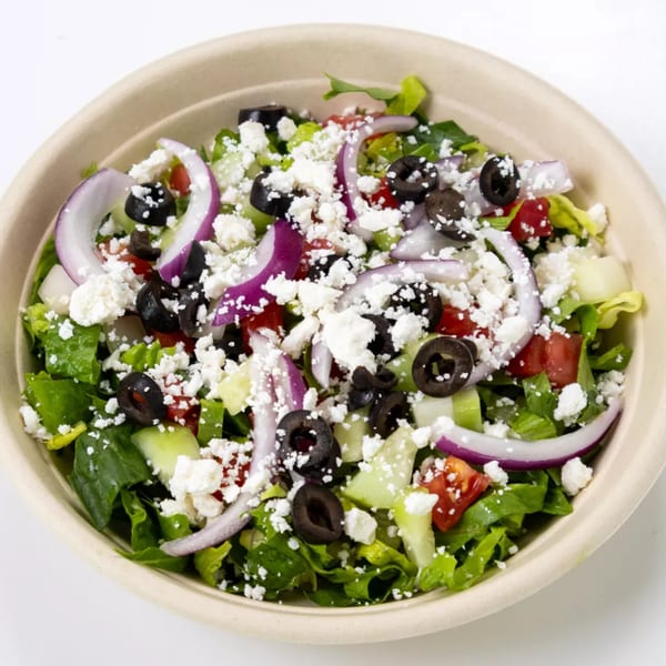 A vibrant Greek salad with lettuce, tomatoes, cucumbers, red onions, black olives, and feta cheese.