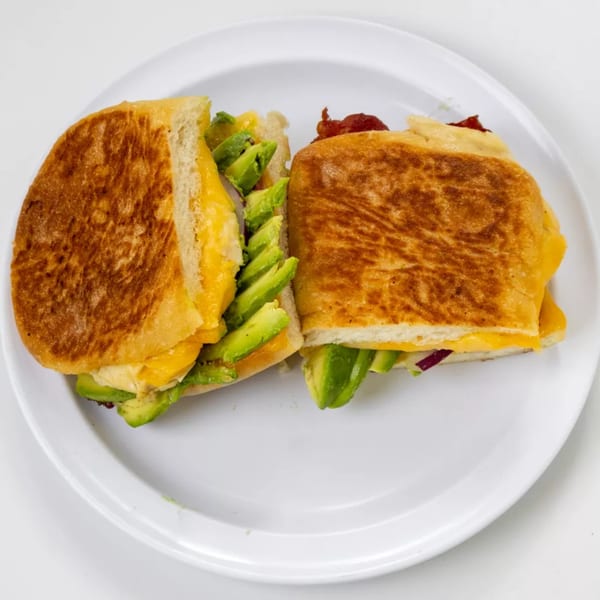 Toasted sandwich halves with melted cheese, sliced avocado, and bacon on a white plate.