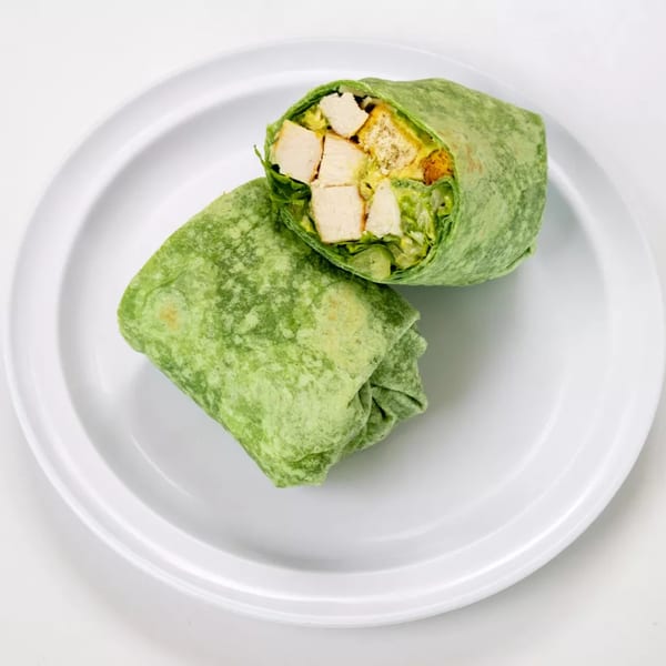 Two green wraps filled with chicken and lettuce, one cut open, on a white plate.