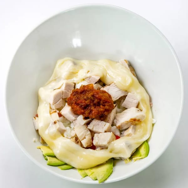 A white bowl filled with diced chicken, melted cheese, salsa, and sliced avocado.