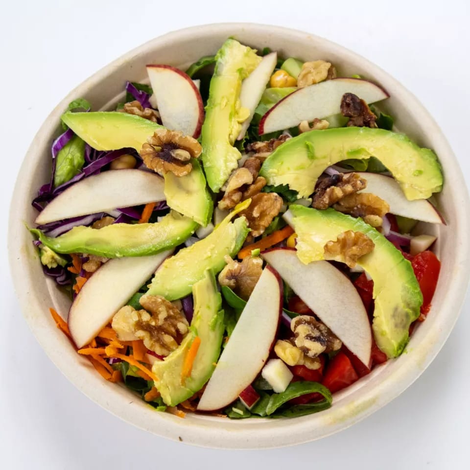 Colorful salad with avocado slices, apple wedges, walnuts, and mixed greens in a bowl.