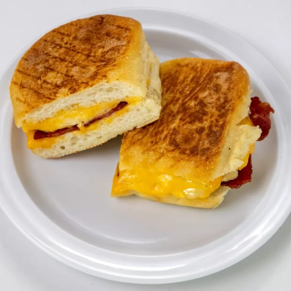 Two halves of a grilled cheese and bacon sandwich on a white plate.