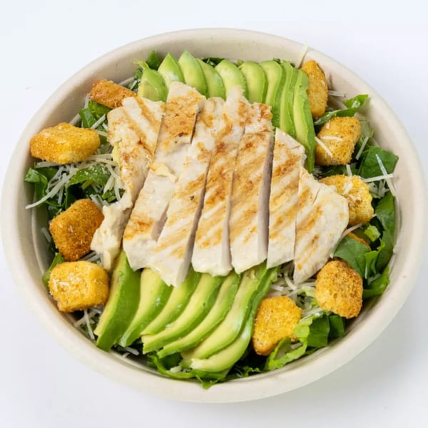 Grilled chicken, sliced avocado, croutons, and shredded cheese on a bed of green lettuce.
