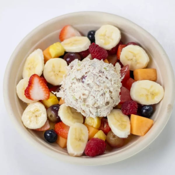 A bowl of fresh fruit salad with a scoop of chicken salad in the center.