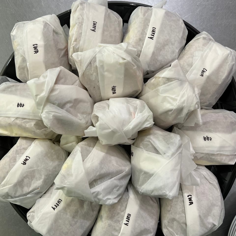 A tray filled with individually wrapped sandwiches, labeled "curry," "tuna," "egg," and "CWA".