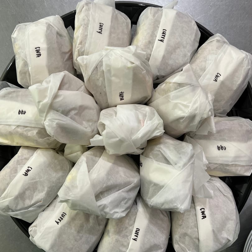 A tray filled with individually wrapped sandwiches, labeled "curry," "tuna," "egg," and "CWA".