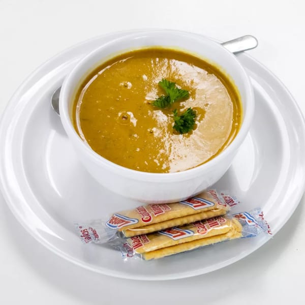 A white bowl of golden-orange soup with parsley garnish, served with crackers on a white plate.